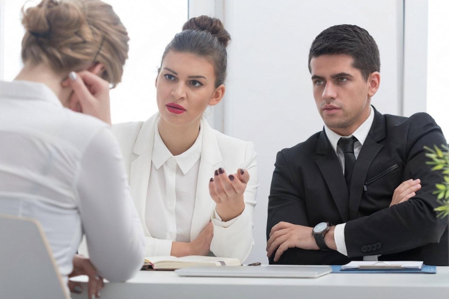 Two managers questioning a female employee across a desk during an internal fraud interview in a UAE office
